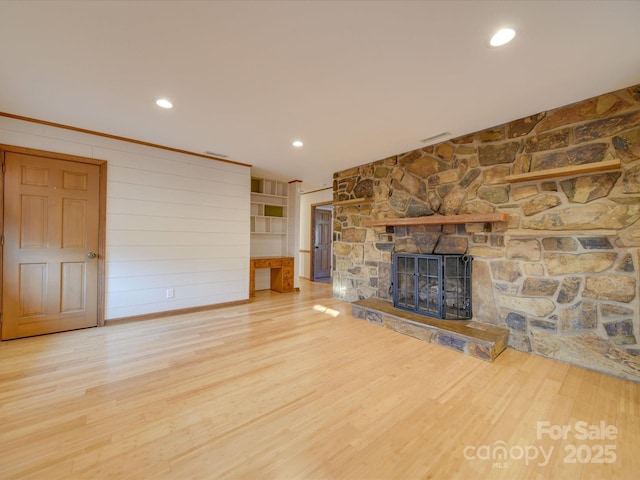 unfurnished living room with hardwood / wood-style floors, ornamental molding, and a stone fireplace