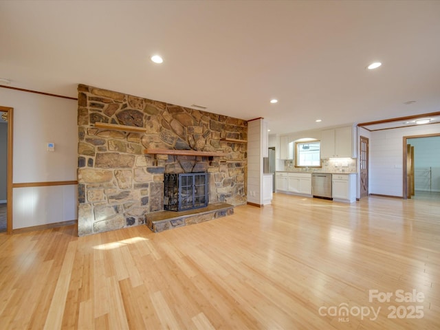 unfurnished living room with crown molding, a stone fireplace, and light wood-type flooring