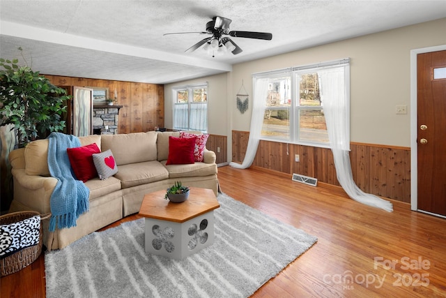 living room with a textured ceiling, wood walls, ceiling fan, and a wealth of natural light