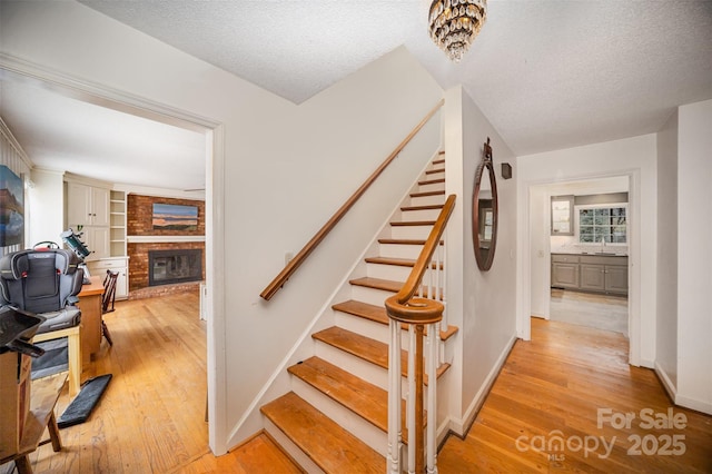 stairs with a brick fireplace, wood-type flooring, and a textured ceiling