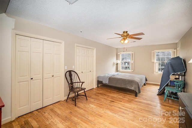 bedroom featuring light hardwood / wood-style flooring, ceiling fan, a textured ceiling, and two closets