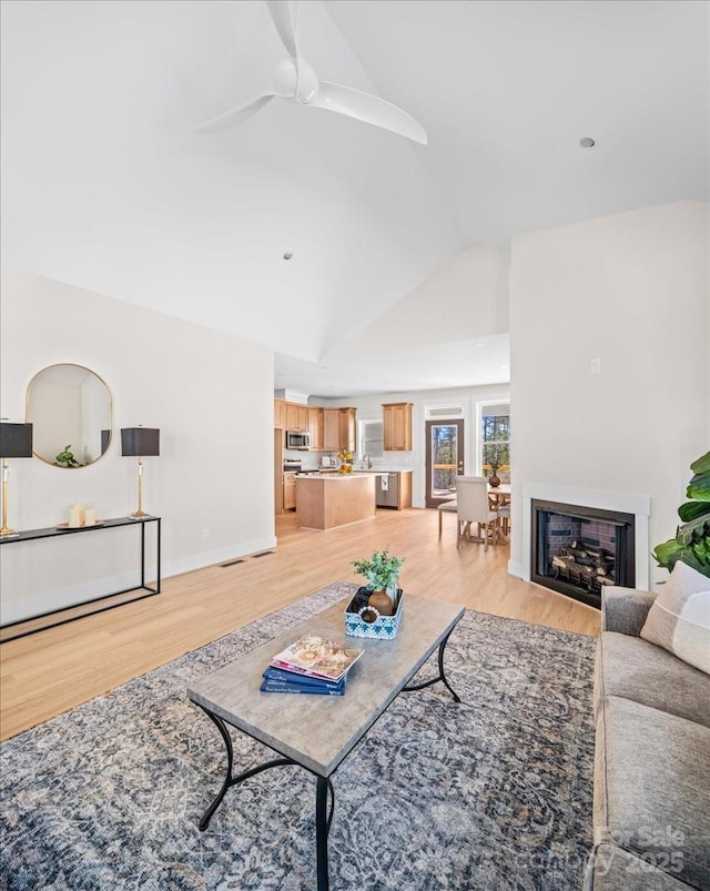 living room with high vaulted ceiling, ceiling fan, and light hardwood / wood-style flooring