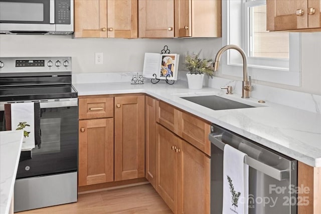 kitchen featuring light stone countertops, appliances with stainless steel finishes, light hardwood / wood-style floors, and sink