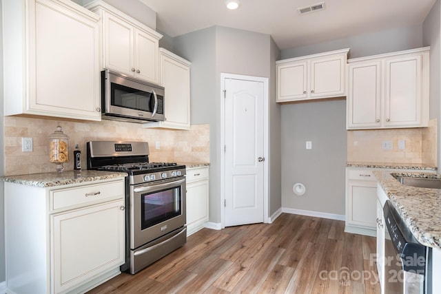 kitchen with white cabinets, backsplash, appliances with stainless steel finishes, and light stone counters