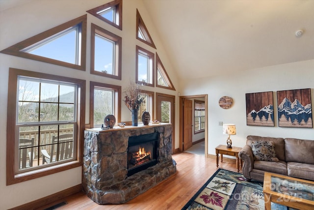 living room featuring high vaulted ceiling, a healthy amount of sunlight, a fireplace, and light hardwood / wood-style floors