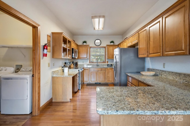 kitchen featuring sink, light hardwood / wood-style flooring, appliances with stainless steel finishes, independent washer and dryer, and light stone countertops