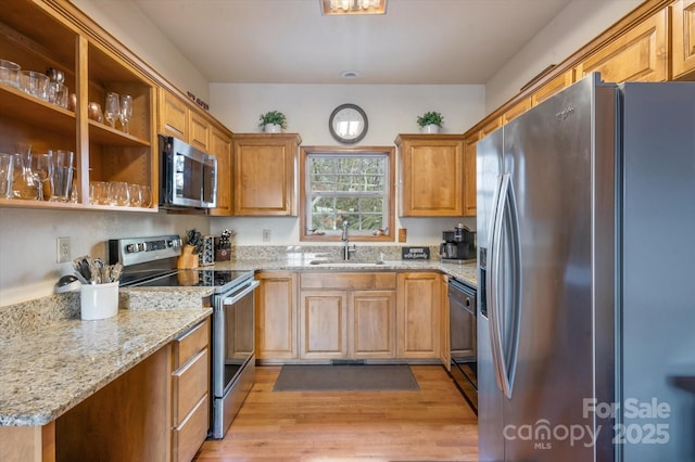 kitchen with light stone counters, stainless steel appliances, sink, and light hardwood / wood-style flooring