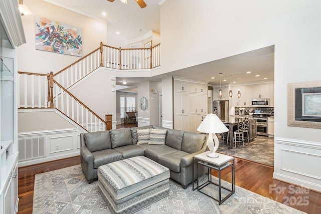 living room with ceiling fan, ornamental molding, dark hardwood / wood-style flooring, and a high ceiling