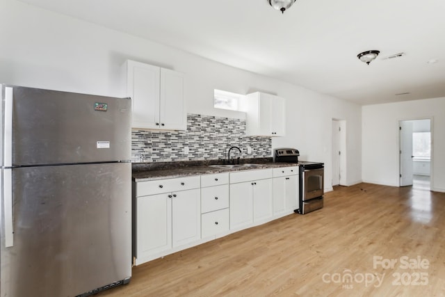 kitchen with appliances with stainless steel finishes, white cabinetry, light hardwood / wood-style floors, sink, and backsplash