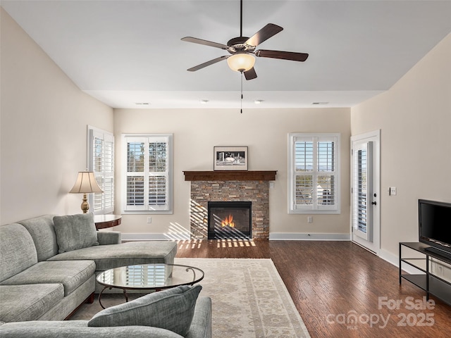 living room with ceiling fan, dark hardwood / wood-style floors, and a stone fireplace