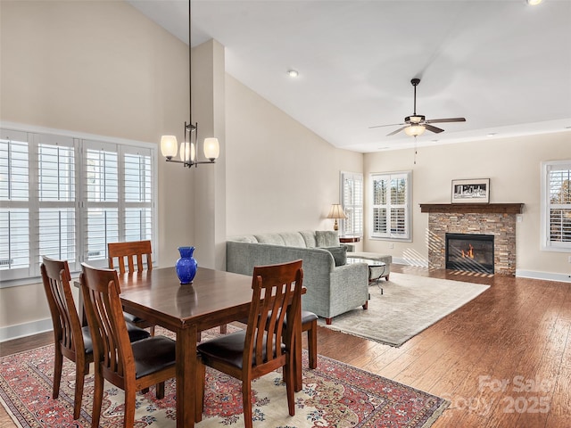 dining room with ceiling fan with notable chandelier, vaulted ceiling, a fireplace, and hardwood / wood-style flooring