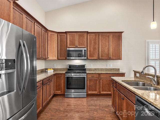 kitchen with a high ceiling, stainless steel appliances, hanging light fixtures, light stone countertops, and sink