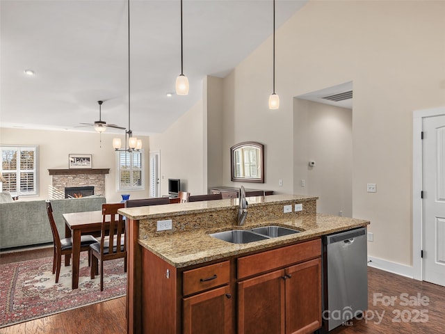 kitchen with dishwasher, decorative light fixtures, sink, a kitchen island with sink, and a stone fireplace