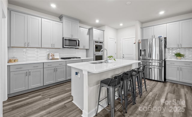 kitchen featuring an island with sink, decorative backsplash, a breakfast bar area, appliances with stainless steel finishes, and sink