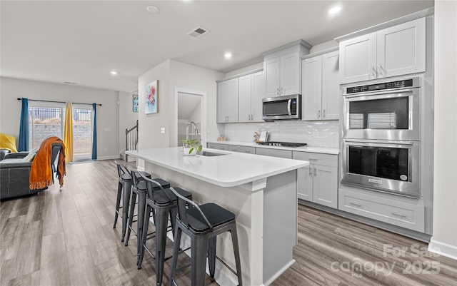 kitchen featuring sink, a kitchen breakfast bar, decorative backsplash, a center island with sink, and appliances with stainless steel finishes