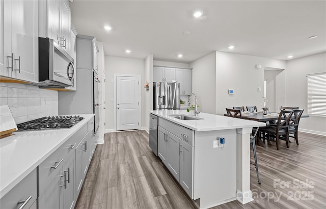 kitchen featuring gray cabinets, a center island with sink, appliances with stainless steel finishes, light wood-type flooring, and sink