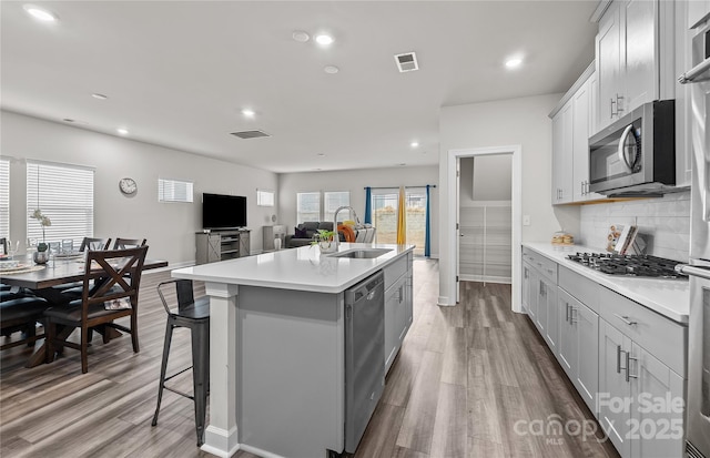 kitchen with a center island with sink, decorative backsplash, light wood-type flooring, appliances with stainless steel finishes, and sink