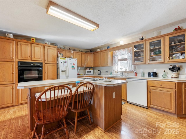 kitchen featuring a kitchen island, a kitchen bar, white appliances, a textured ceiling, and light wood-type flooring