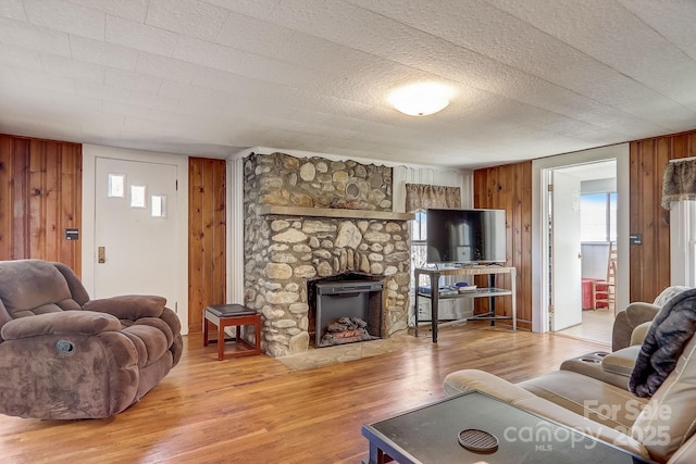 living room with wooden walls, hardwood / wood-style floors, and a stone fireplace