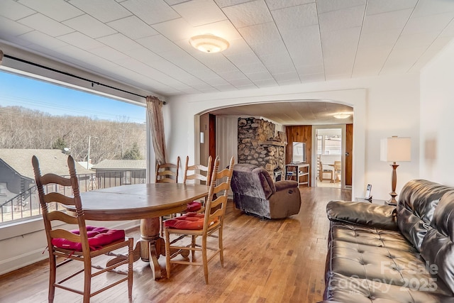 dining space featuring wood walls, light hardwood / wood-style flooring, a healthy amount of sunlight, and a stone fireplace