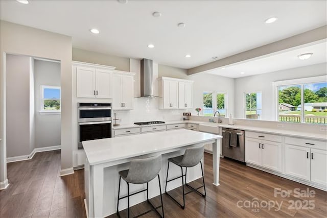 kitchen featuring appliances with stainless steel finishes, white cabinetry, a kitchen island, and wall chimney exhaust hood