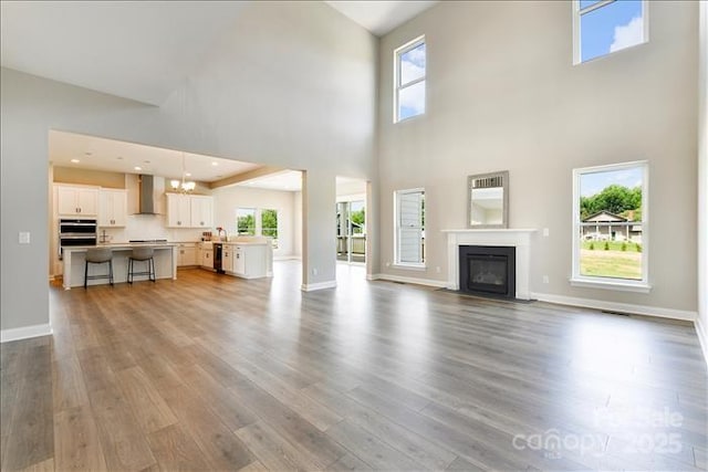 unfurnished living room featuring a high ceiling, a notable chandelier, hardwood / wood-style floors, and plenty of natural light