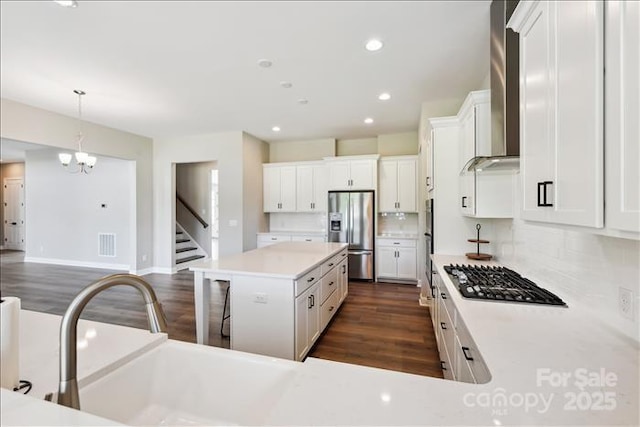 kitchen with appliances with stainless steel finishes, wall chimney exhaust hood, a kitchen island, white cabinetry, and decorative light fixtures