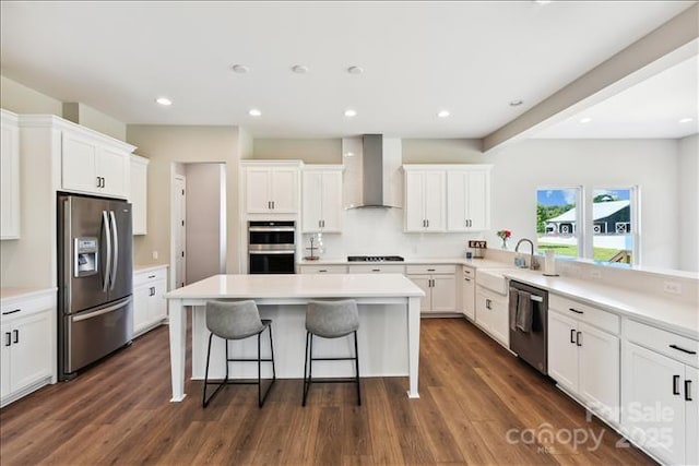 kitchen with stainless steel appliances, a kitchen bar, a kitchen island, wall chimney exhaust hood, and white cabinetry