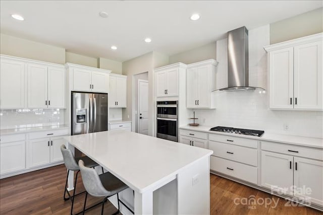 kitchen with stainless steel appliances, wall chimney exhaust hood, backsplash, and white cabinetry