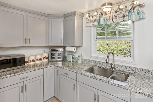 kitchen with sink, light stone counters, and gray cabinets