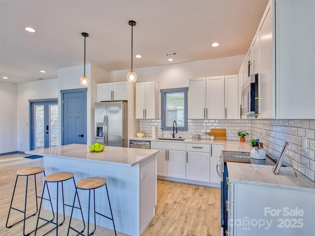 kitchen featuring pendant lighting, a kitchen island, white cabinets, appliances with stainless steel finishes, and sink