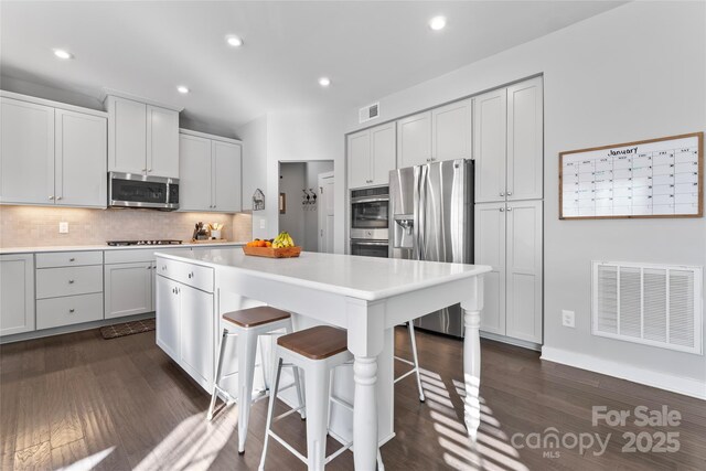 kitchen with appliances with stainless steel finishes, dark hardwood / wood-style flooring, white cabinets, a breakfast bar, and a center island