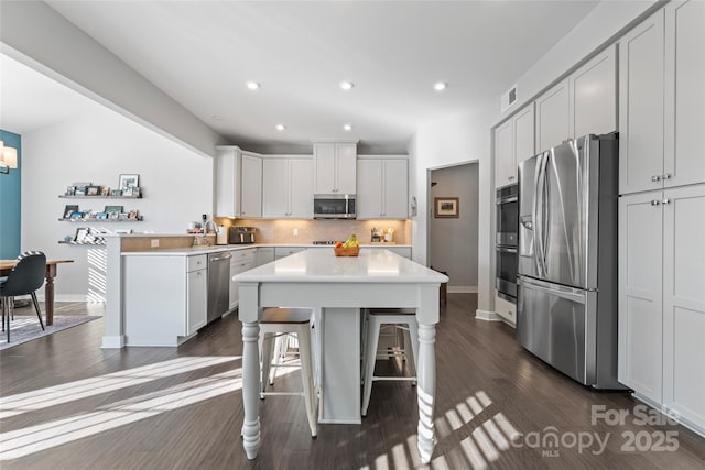 kitchen with a center island, a breakfast bar, white cabinetry, dark wood-type flooring, and appliances with stainless steel finishes