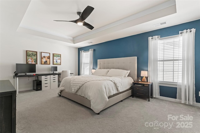 bedroom with a raised ceiling, light colored carpet, and ceiling fan