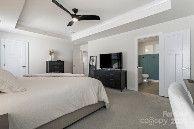 carpeted bedroom with ensuite bathroom, ceiling fan, and a tray ceiling