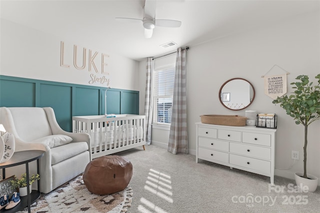 carpeted bedroom with ceiling fan and a nursery area