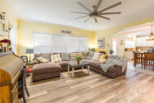 living room with ceiling fan with notable chandelier, ornamental molding, sink, and light hardwood / wood-style floors