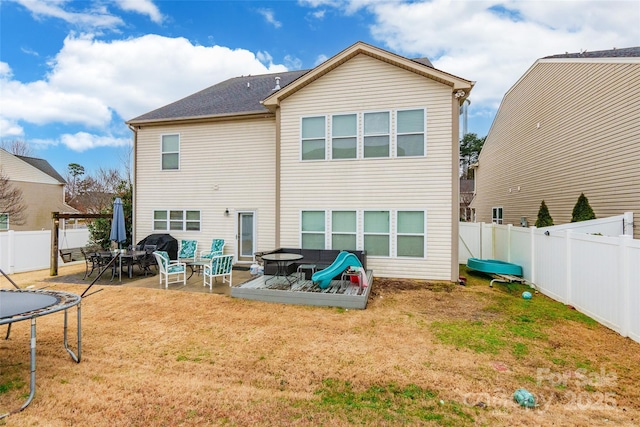 rear view of house featuring a trampoline, a yard, and a patio