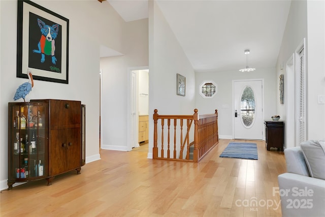 entryway featuring light wood finished floors, a chandelier, baseboards, and high vaulted ceiling