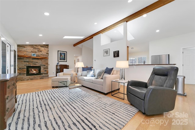 living room featuring light wood-style flooring, a stone fireplace, recessed lighting, and a skylight