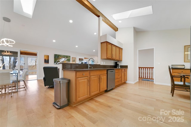 kitchen featuring a skylight, stainless steel dishwasher, dark countertops, beam ceiling, and light wood finished floors