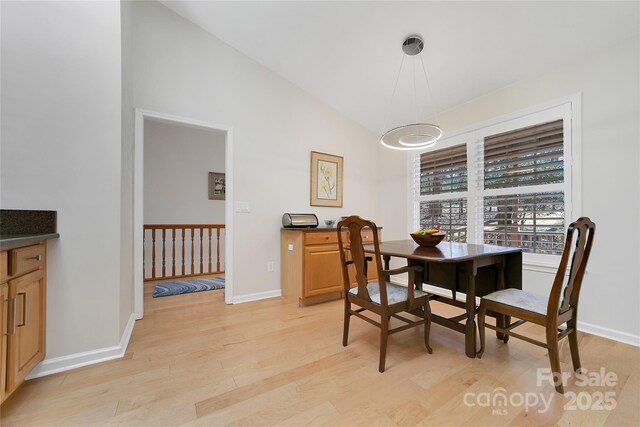 dining room with light wood finished floors, baseboards, and vaulted ceiling