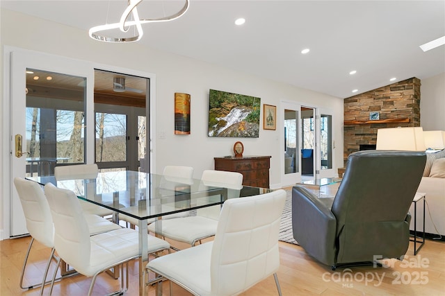 dining area with light wood-style flooring, a chandelier, a stone fireplace, recessed lighting, and lofted ceiling