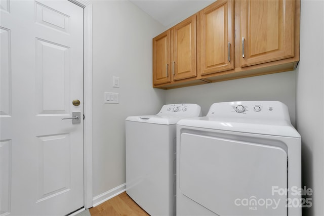 laundry room featuring washing machine and dryer, cabinet space, baseboards, and light wood-style flooring