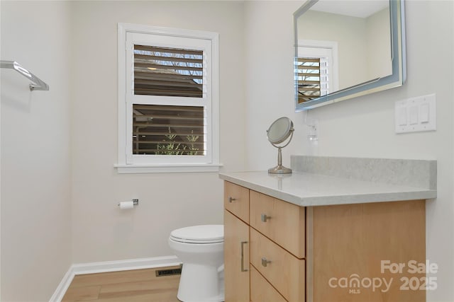 half bathroom with baseboards, wood finished floors, vanity, and toilet