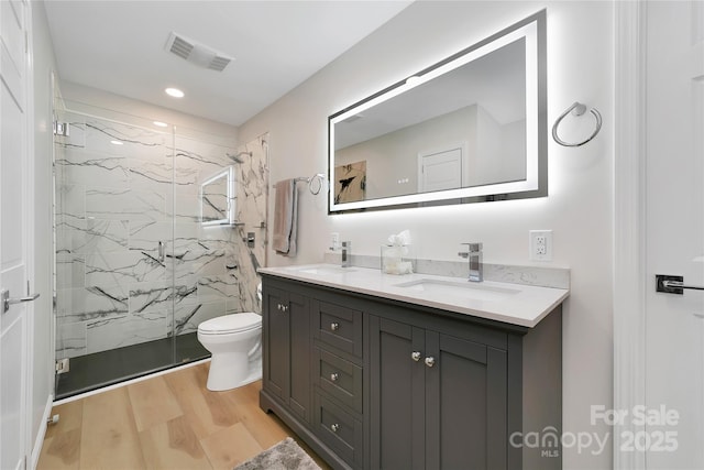 full bath featuring wood finished floors, a marble finish shower, double vanity, toilet, and recessed lighting