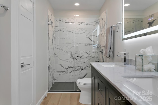 bathroom with a marble finish shower, double vanity, toilet, wood finished floors, and recessed lighting