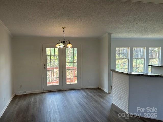 unfurnished dining area with a textured ceiling, a chandelier, ornamental molding, and dark hardwood / wood-style floors