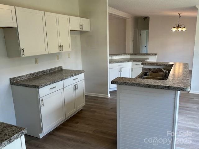 kitchen featuring a notable chandelier, pendant lighting, dark hardwood / wood-style floors, sink, and white cabinetry