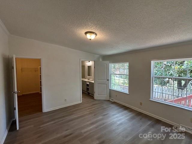 unfurnished bedroom with a textured ceiling, a closet, dark hardwood / wood-style floors, a walk in closet, and ensuite bath